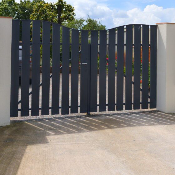 Contemporary driveway gate with vertical steel slats and curved top