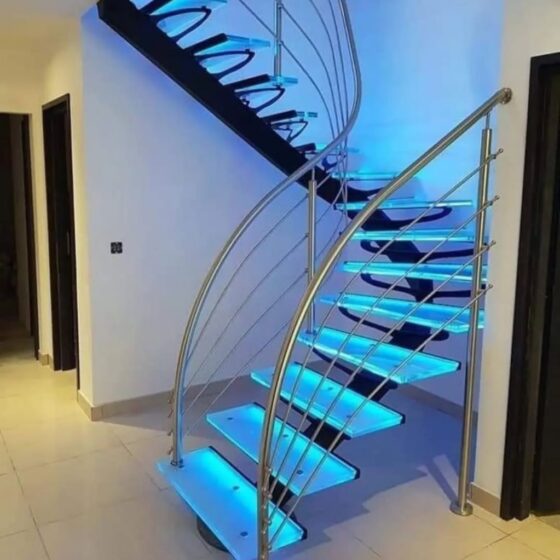 Curved metal staircase with glass treads and blue LED lighting; stainless-steel handrail in a modern interior